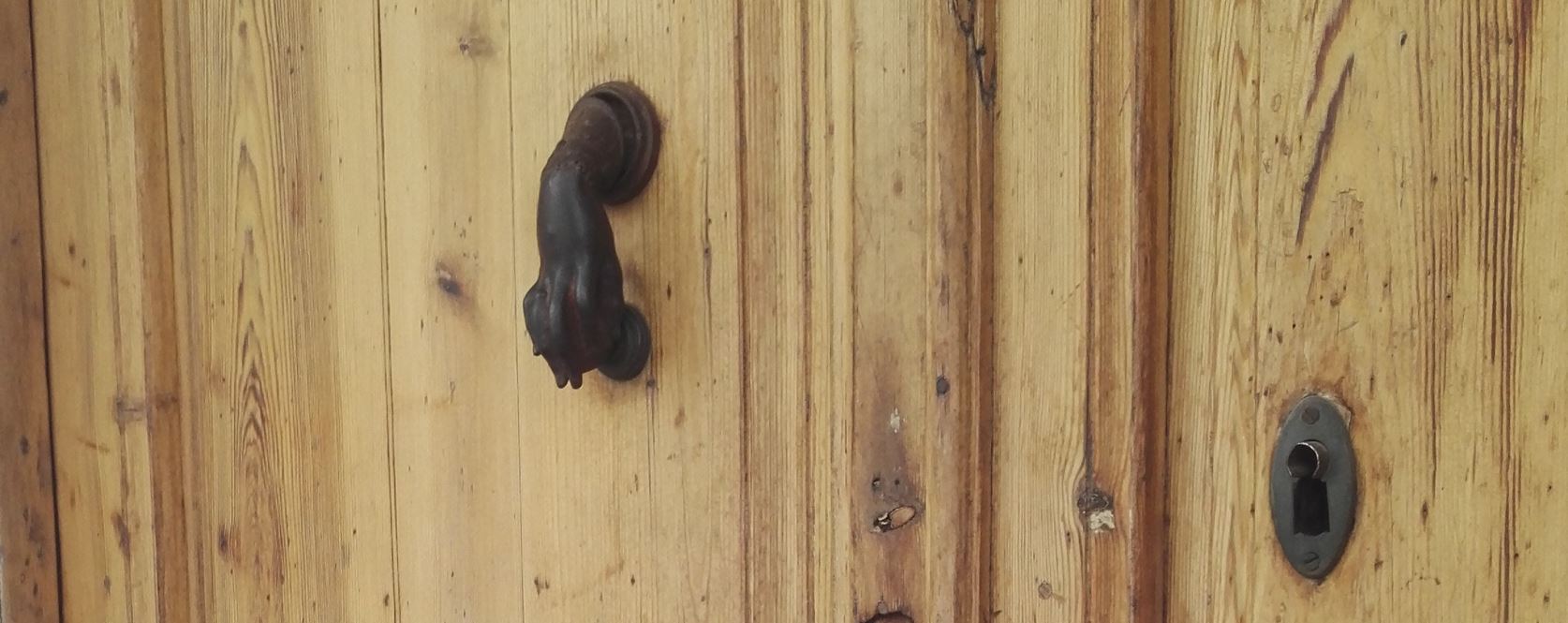 Rajattu kuva puuovesta, jossa on metallinen, tassun muotoinen kolkutin.